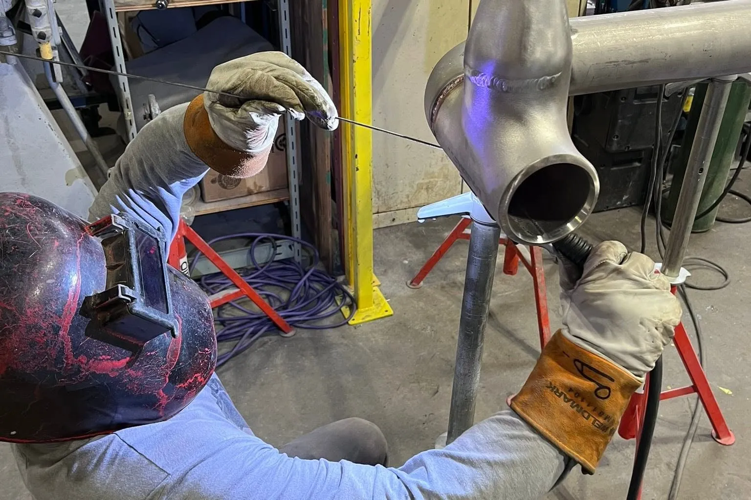 Chris welding a stainless steel pipe fitting, in his welding hood and leather gloves