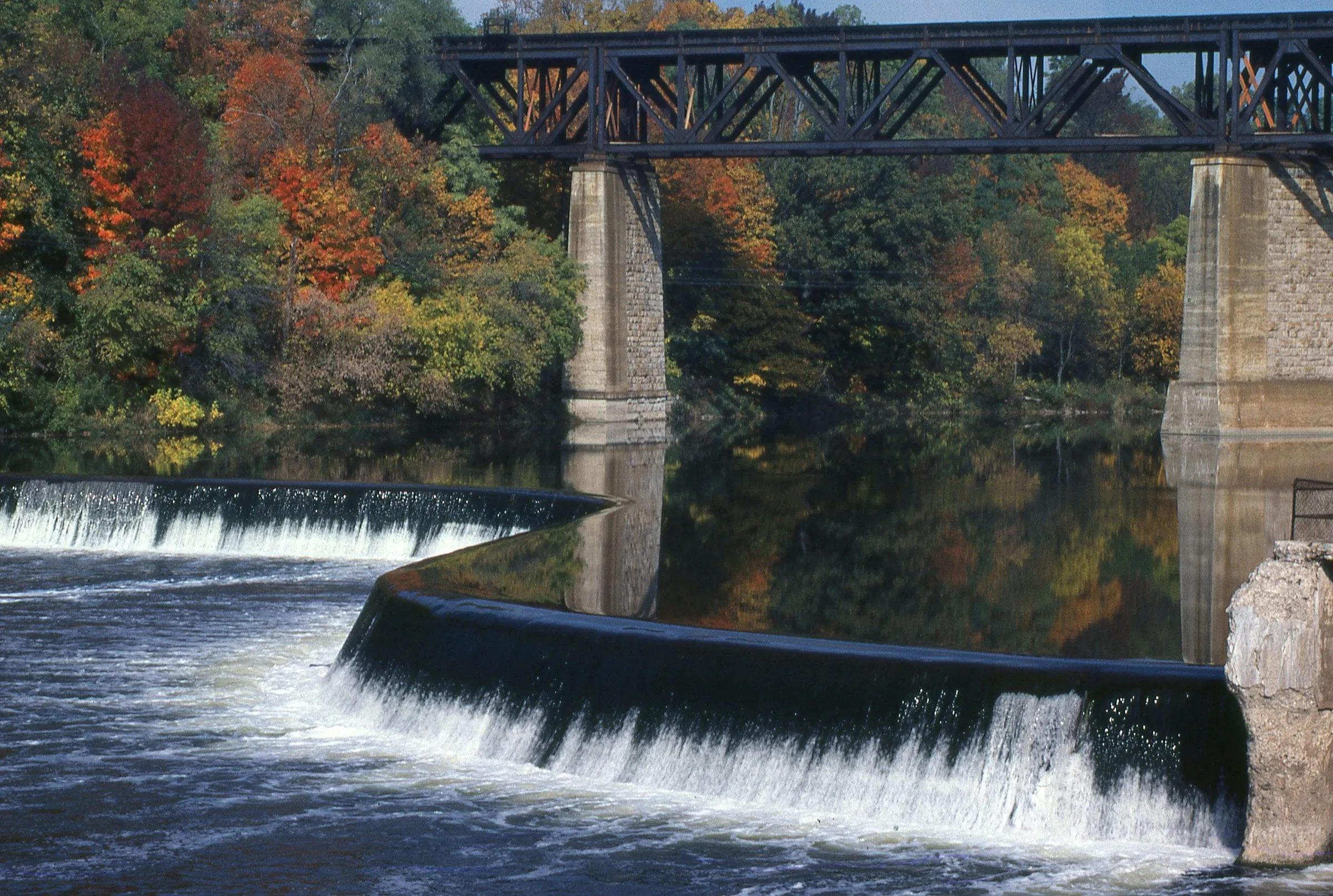 The rail bridge and the curved dam on the Grand River at Paris, autumn trees along the banks