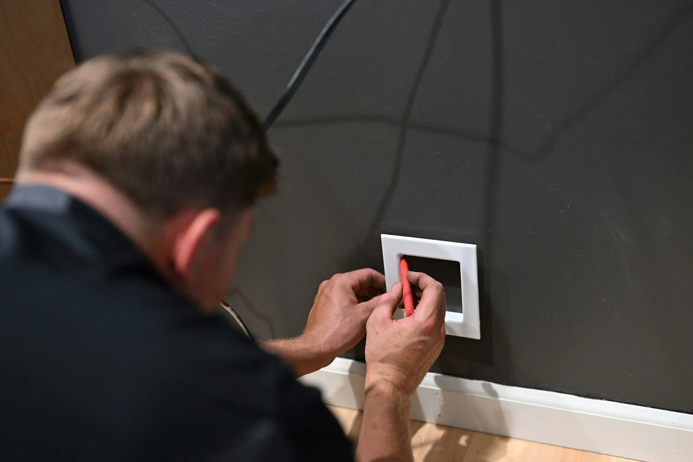 A tradesman tracing the outline of a box on a kitchen wall before cutting
